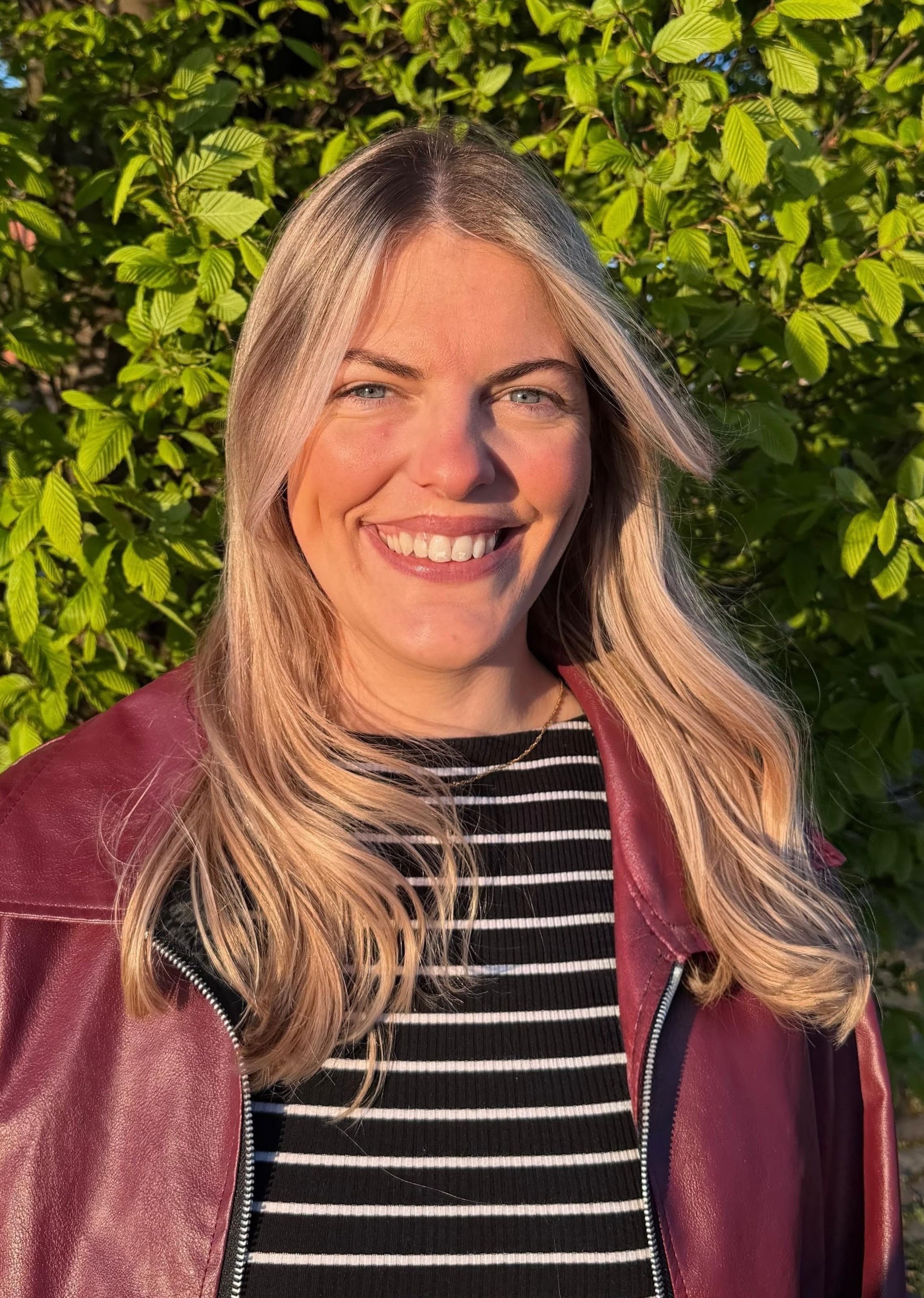 Sian Armstrong smiling in front of a tree in evening sunlight